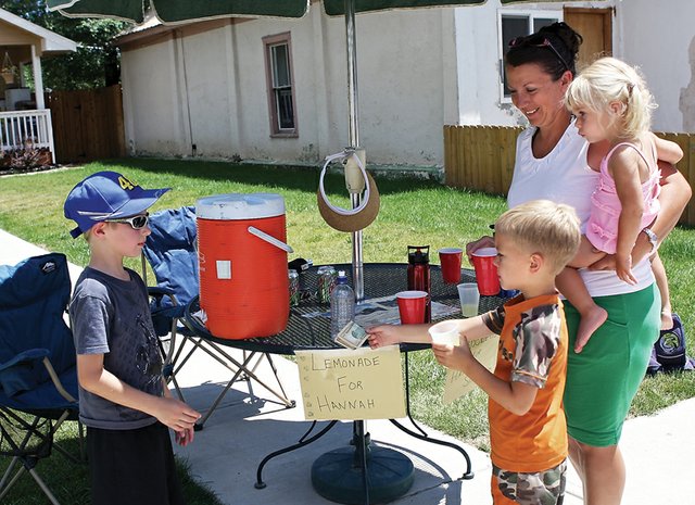 Tyler Burkett, 7, sells lemonade to Kody Feldmann, 5, his mother, Amy, and his sister, Kylie, 2, on Friday on Yampa Avenue. Tyler and his sister, Brianna, 9, operated the stand to raise money for former Craig resident Hannah Sixkiller, 7, who is being treated for brain cancer. The Feldmanns, who are Hannah’s neighbors from Dixon, Wyo., came to Craig to use the community swimming pool, and noticed the stand while driving into town.