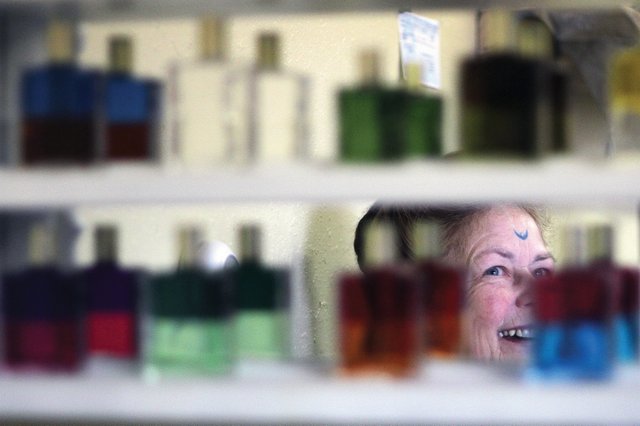 Craig resident Sharon Miller, 66, is reflected Thursday in a mirror display of bottles of color therapy, which is an oil and water mixture and serves as part of soul readings that Miller provides as part of her work at the store. Miller opened her store, Crystal Sanctuary, Nov. 26 and said business has been good.