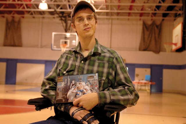Steven Sharp, 21, sits in a wheelchair Sunday at the Boys & Girls Club of Craig holding a picture of himself on life support at St. Mary’s Hospital in Grand Junction. Sharp spent six months in the hospital after a June 26 motocross crash caused traumatic brain injuries. He returned home Sunday, and friends and family hosted a reception to welcome him back.