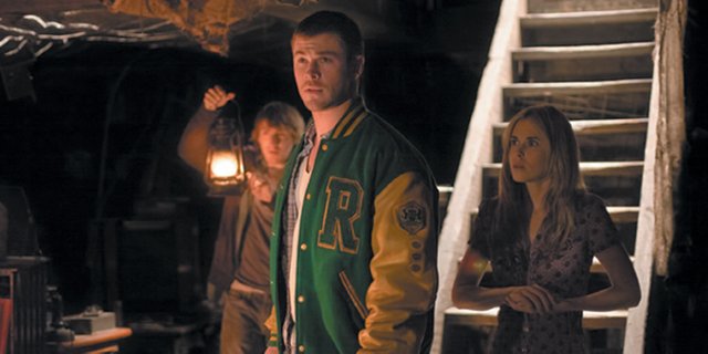 From left, college students Marty (Fran Kranz), Curt (Chris Hemsworth) and Jules (Anna Hutchison) cautiously walk into the darkness of the creepy cellar of their vacation retreat in “The Cabin in the Woods.” The movie is about five young people who find themselves involved in a deadly ritual when they travel to a remote nature location.