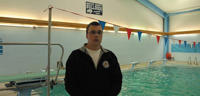 Moffat County High School senior John Kirk stands proudly beneath the American flag at the MCHS pool. Kirk, the captain of the boys varsity swim team, will be attending the United States Merchant Marine Academy in the fall, where he will row crew for the military institute. The jacket he is wearing has the USMMA insignia on the front.