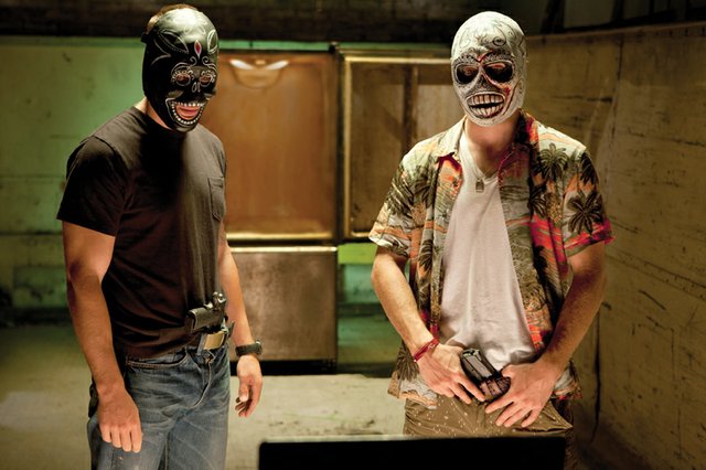 Drug dealers Chon (Taylor Kitsch), left, and Ben (Aaron Johnson) don Santa Muerte masks as they speak with rival drug peddlers via webcam in “Savages.” The movie is about two best friends in the marijuana business who are threatened by a Mexican cartel, leading to an escalating war between the two sides.