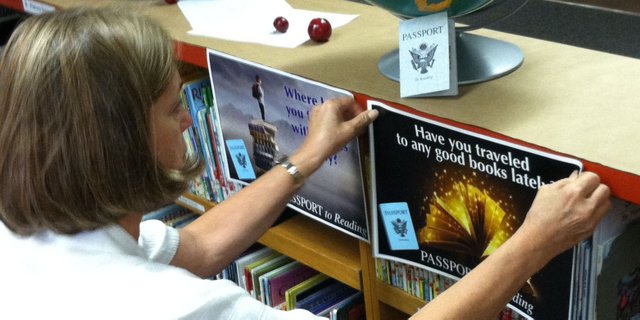 Librarian Bonnie Thompson, of Sunset Elementary School, hangs a sign and sets up a display in anticipation of the Passport to Reading program. The program, for fourth and fifth graders, aims to encourage students to read books from different genres, and not just ones they are comfortable with. Upon reading books, students receive stamps in their "passports." 