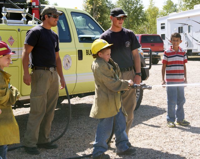 Connor Winn, of Sunset Elementary, takes his turn to spray the hose, as firefighters Hawk Fick, left, and Alex Farinetti of the Craig Bureau of Land Management look on. Fifth graders from Sunset and East Elementary schools took part in an overnight outdoor education experience Thursday and Friday at Yampa River State Park.