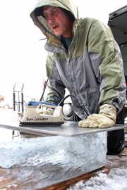Buddy Cassaday places a sheet of aluminum, which was warmed by an iron, on top of a block of ice Thursday. The warmed aluminum smoothes and levels the ice surface so laminated logos can be sealed between two flush blocks of ice.
