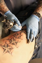 Jimmy Clark uses a rare tattoo machine made of Gibeon Metiorite while working on Justin Donnel’s wind bars Thursday at Liquid Flesh Tattoo.